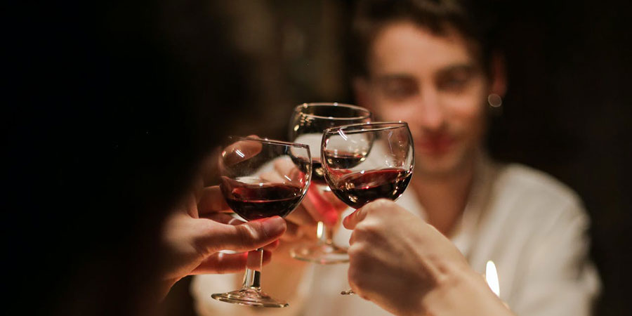 people holding and toasting their wine glasses half filled with red wine